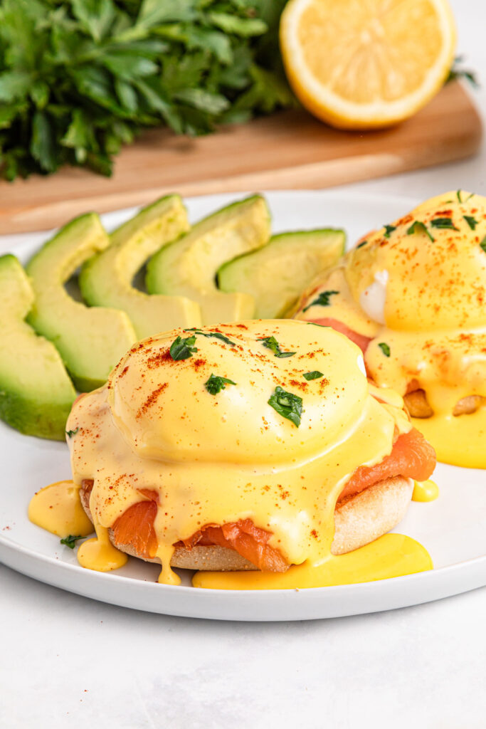 smoked salmon eggs benedict on white plate with sliced avocado