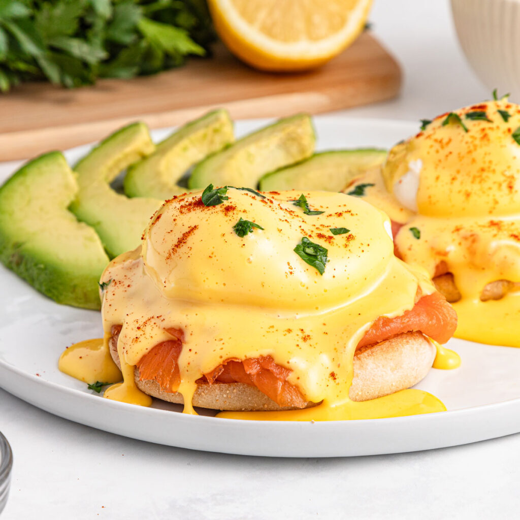 smoked salmon eggs benedict with sliced avocado on white plate