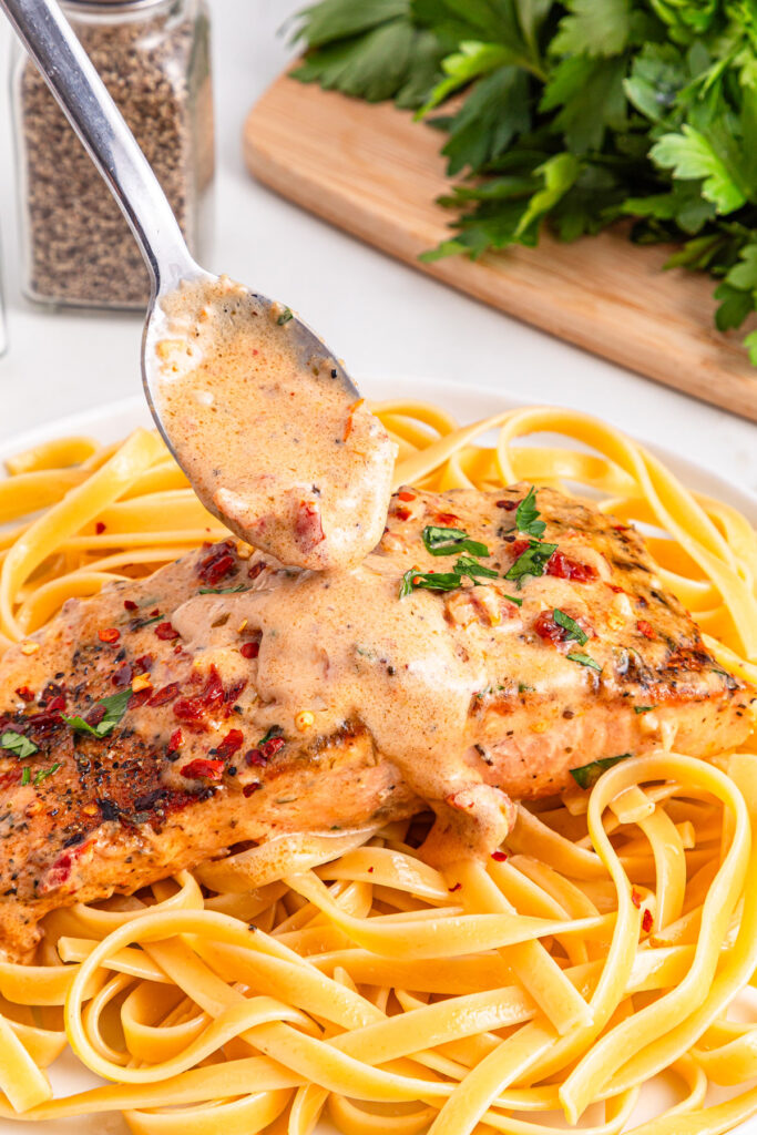 spooning sauce over marry me salmon and linguine