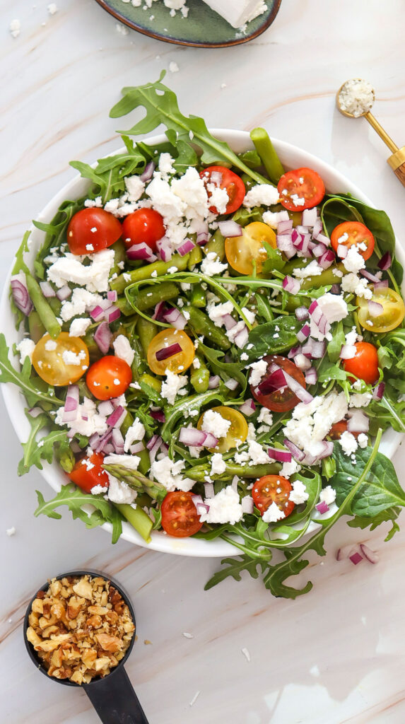 goat cheese asparagus salad in bowl with cup of nuts nearby