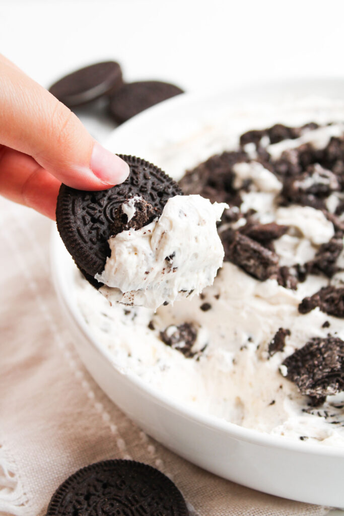 hand dipping oreo cookie into oreo cheesecake dip