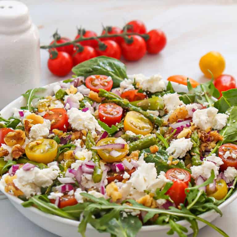 goat cheese asparagus salad in bowl with tomatoes in background