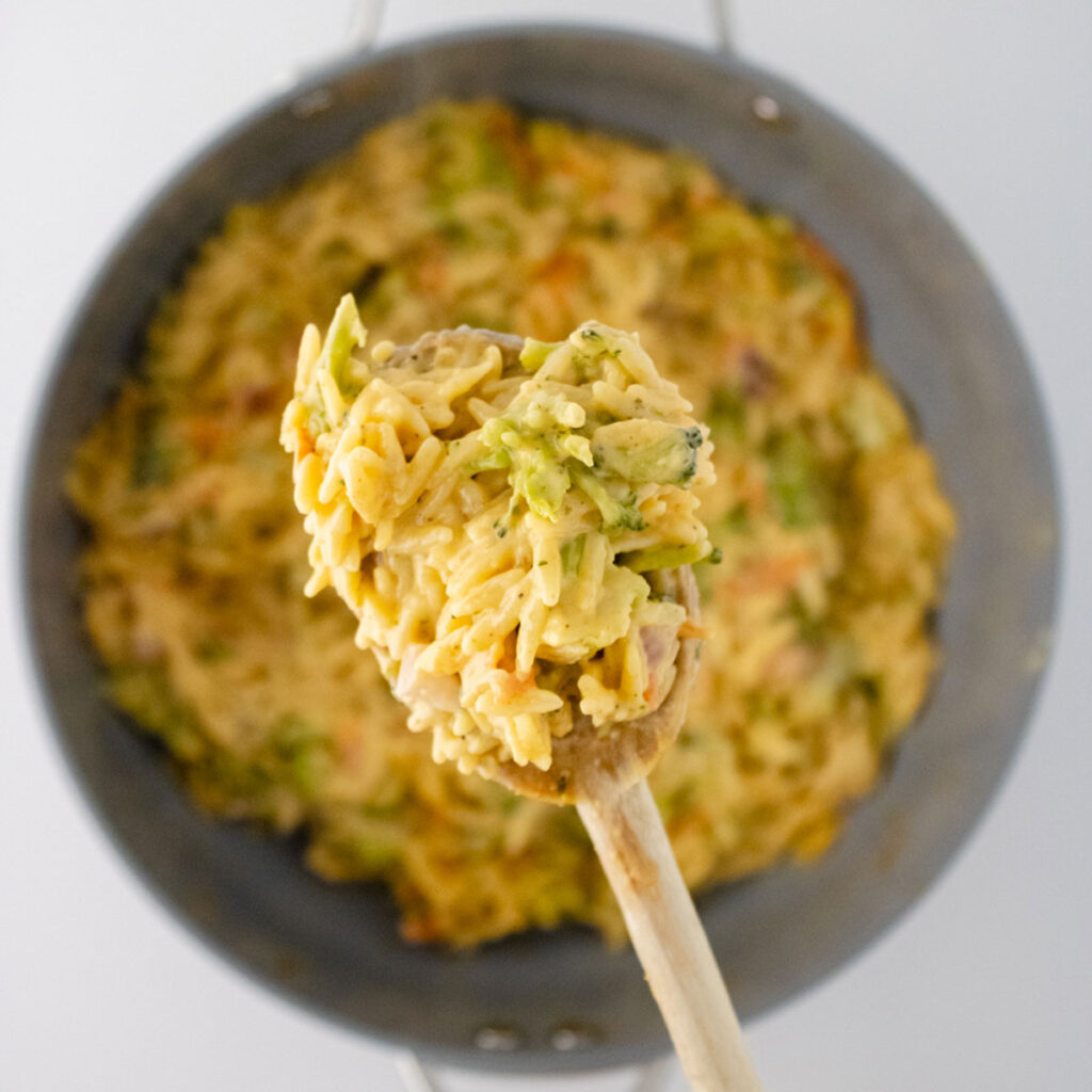 spoonful of broccoli cheddar orzo held over pot of the same