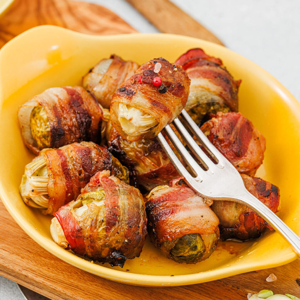 bacon wrapped brussels sprouts in yellow dish with fork in one
