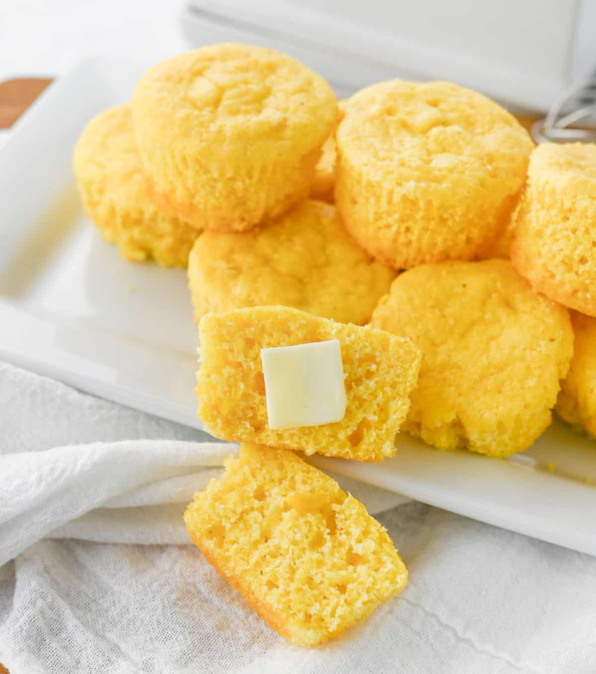 cornbread muffins on white plate with on cut in half with pat of butter