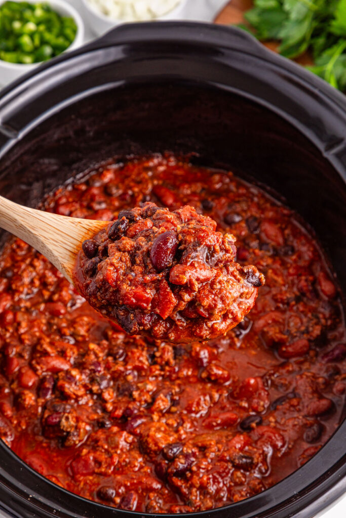 slow cooker with chili and wooden spoon scooping some out