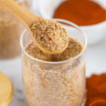 spoon scooping Jamaican jerk seasoning from glass jar