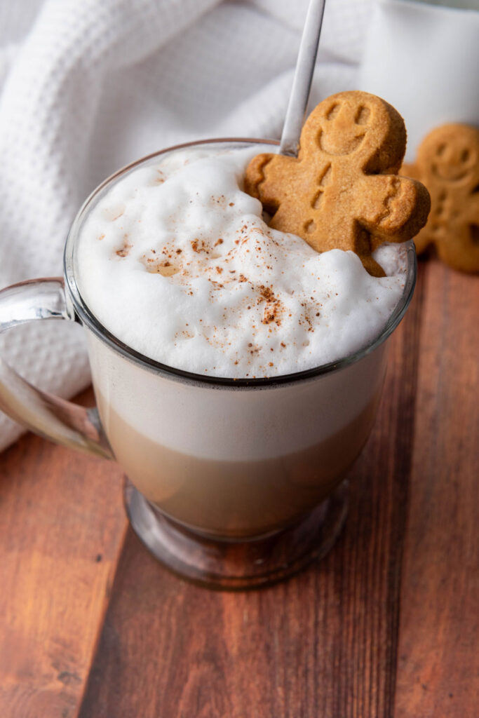 gingerbread latte in glass mug with gingerbread man cookie in frothed milk on top