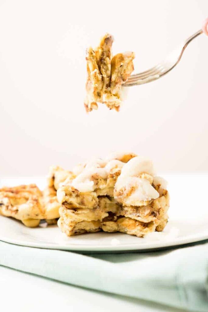fork lifting bite of cinnamon roll waffles from plate