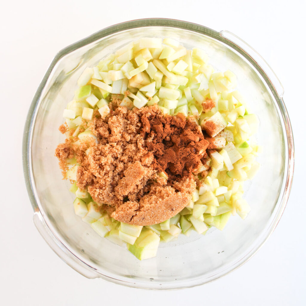 chopped apples with cinnamon and brown sugar in glass bowl