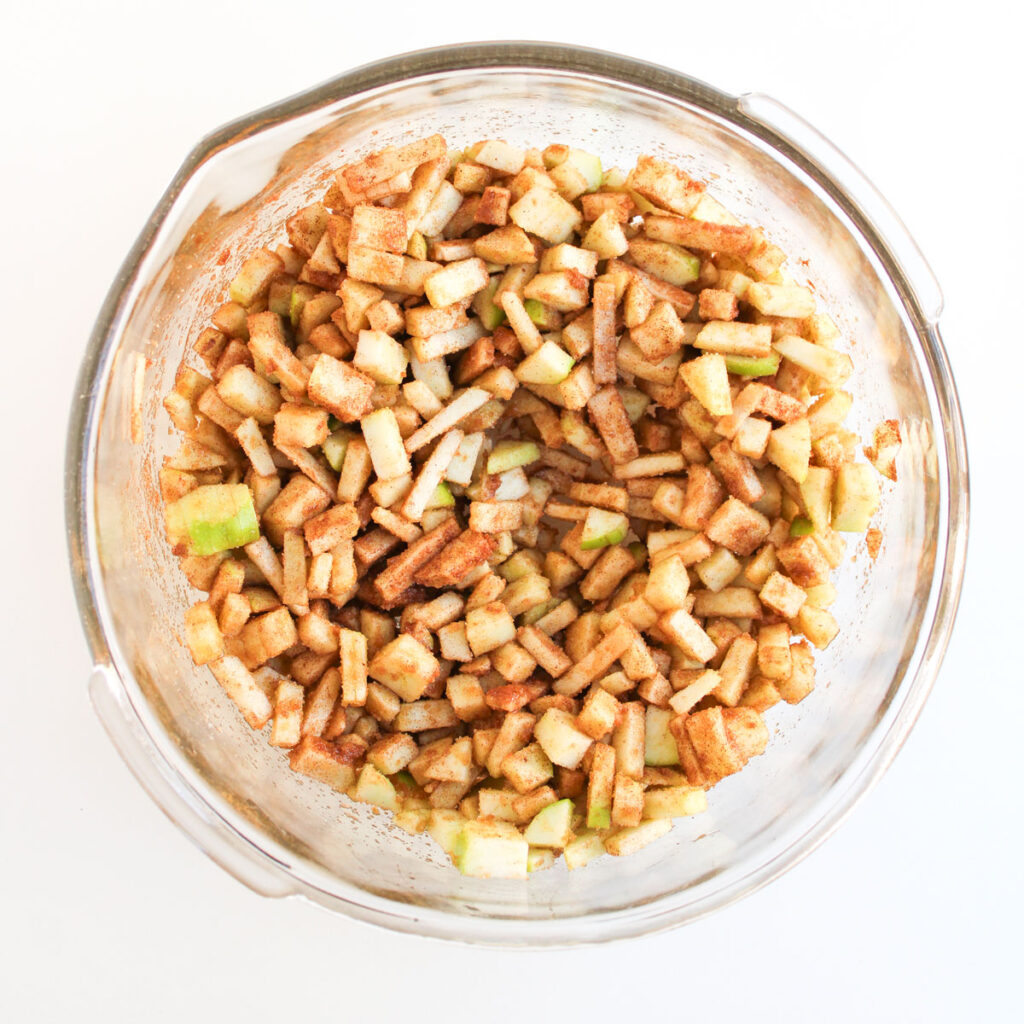 mixing apples with brown sugar and cinnamon in glass bowl