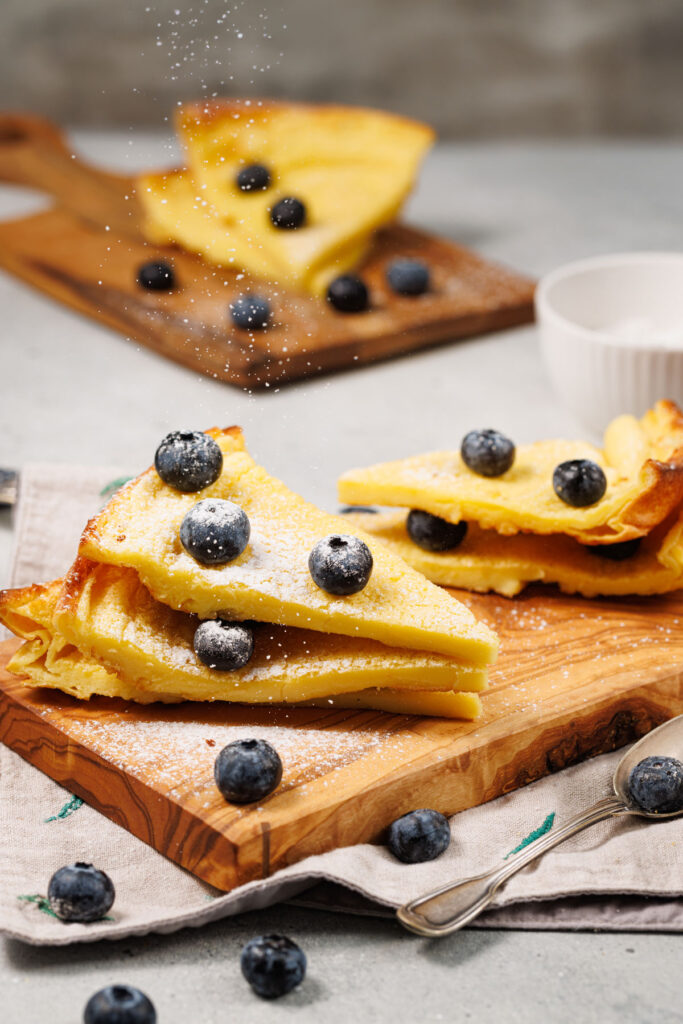 sprinkling powdered sugar over sliced dutch baby pancakes