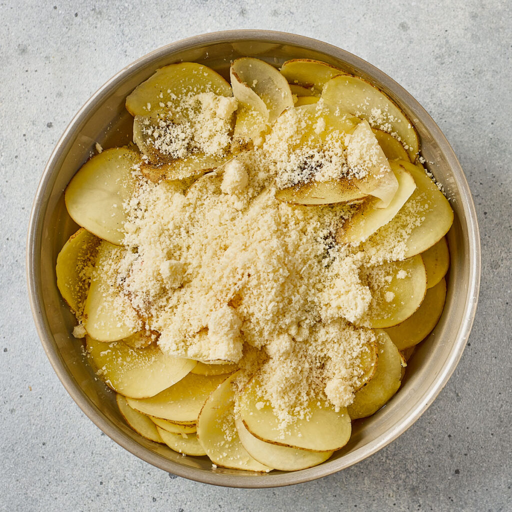 sliced potatoes in bowl with grated parmesan cheese on top
